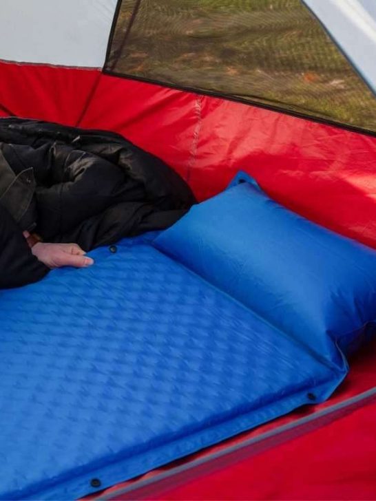 A person setting up their air mattress inside a tent.