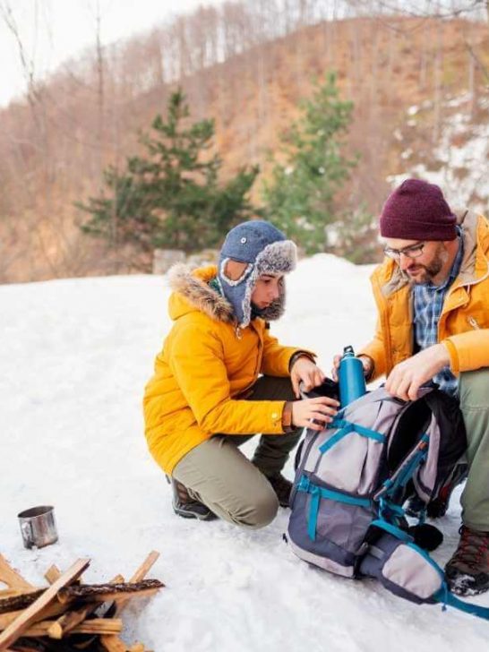 A man and young boy packing a backpack on their campsite in the winter.