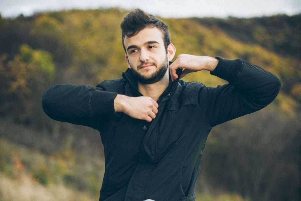 Un hombre quitándose la capa exterior de ropa mientras acampa.